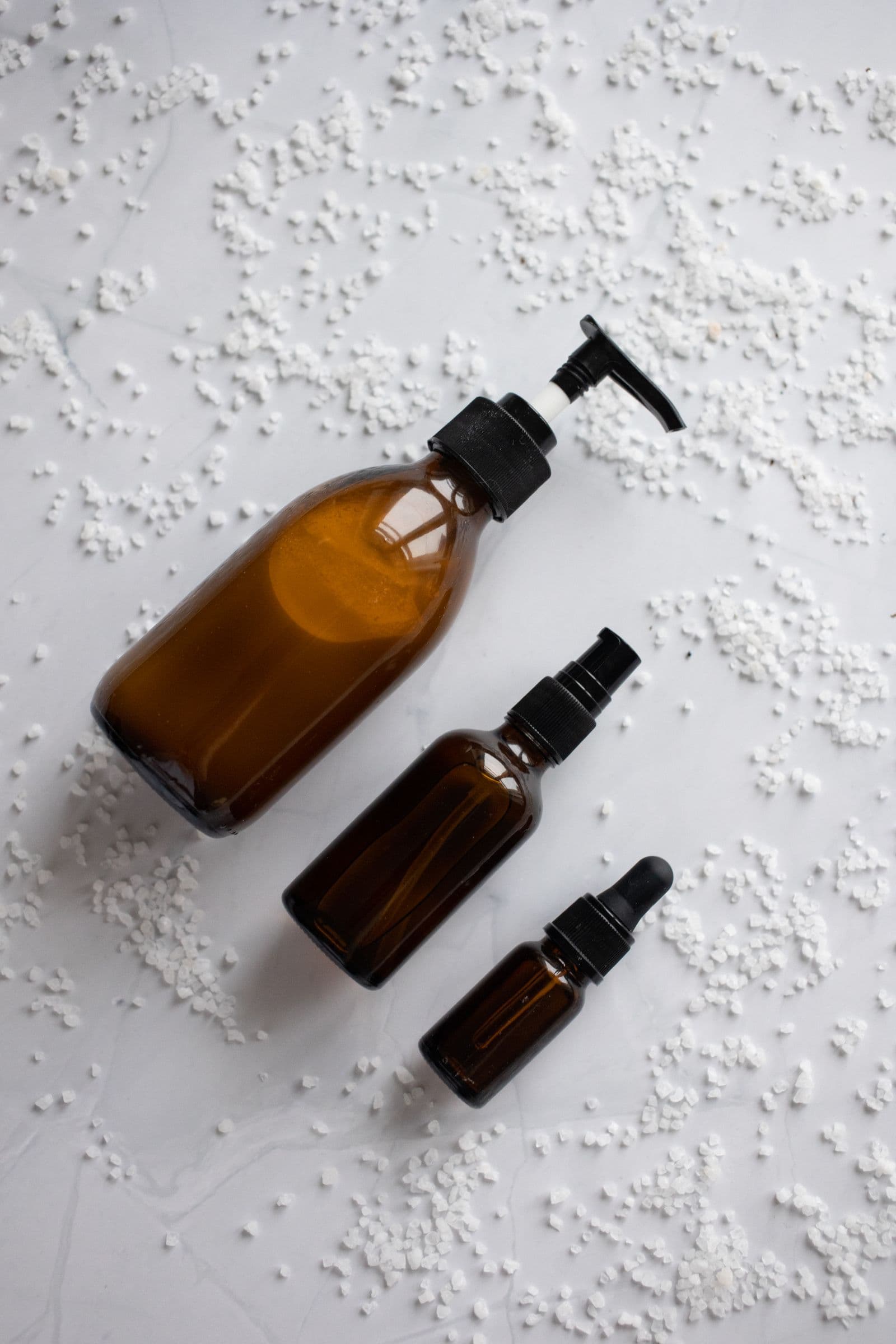 Amber glass spa bottles on marble with scattered bath salts