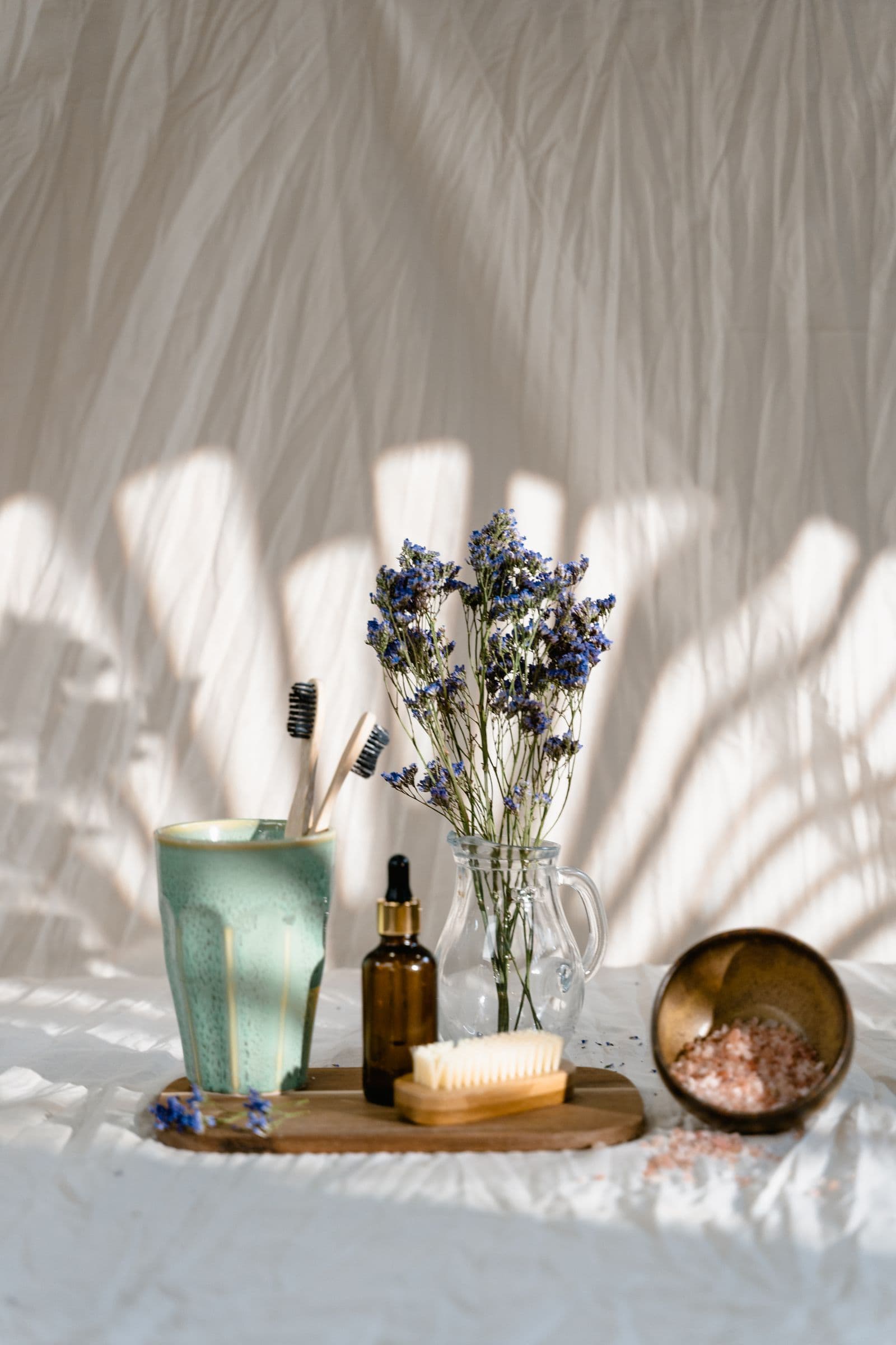 Spa bath essentials on a wooden tray with pink salts and dried flowers