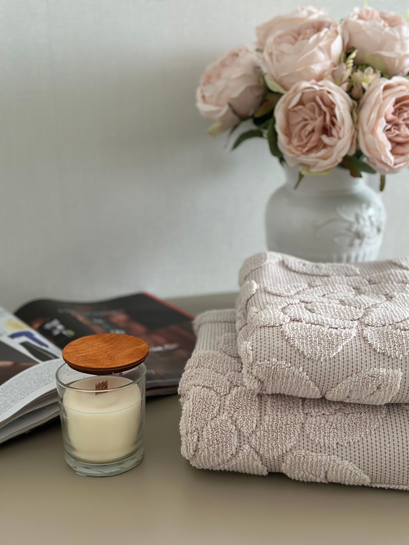 Folded plush towels beside a glass candle and a vase of pale roses